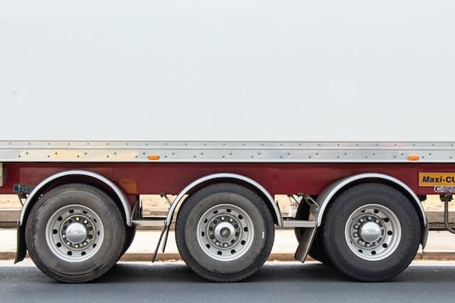 A red flatbed trailer is parked with three visible wheels, situated on a paved road under a clear sky. A yellow sticker on the side reads "max 60 km/h."